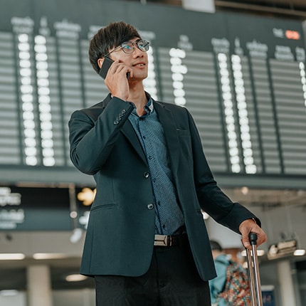 Asian man with suitcase using cellphone at airport